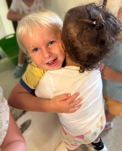 A young boy and girl hug each other closely indoors, with the boy smiling at the camera.