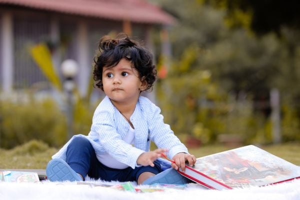 Adorable toddler sitting outdoors enjoying a picture book on a sunny day.