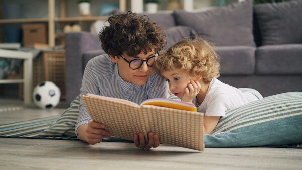 a woman and a child laying on the floor reading a book